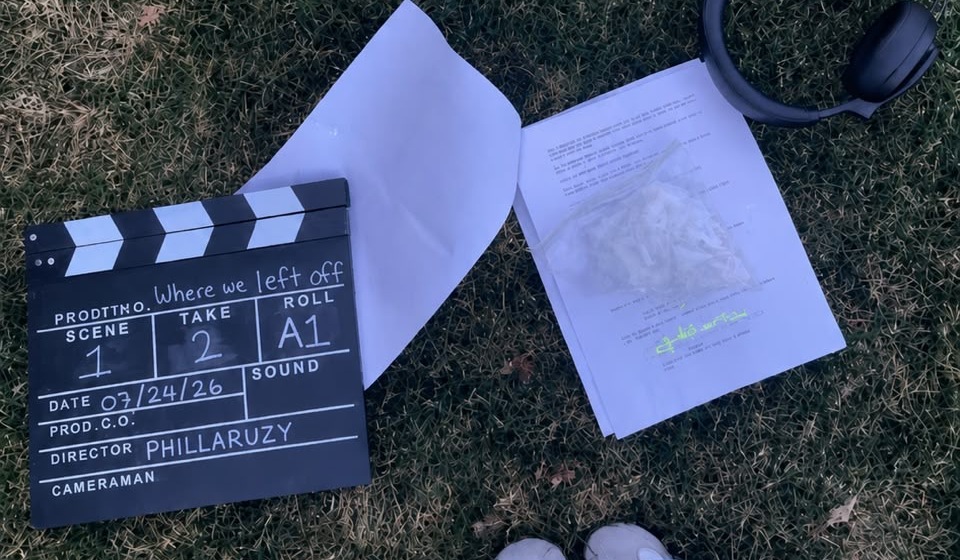 Clapperboard on grass reading 'Where we left off', Scene 1, Take 2, Director Phillaruzy, beside a script and headphones